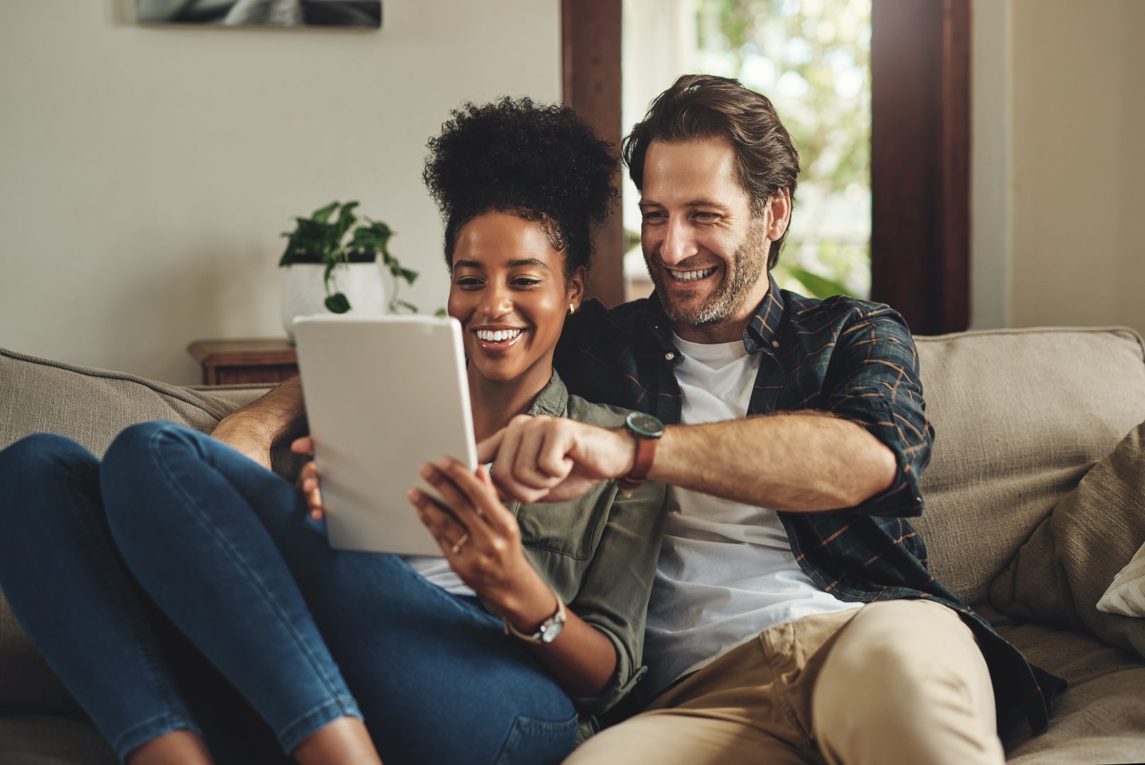 There Are So Many Apps To Choose From. A Happy Young Couple Using A Digital Tablet Together While Relaxing On A Couch At Home.